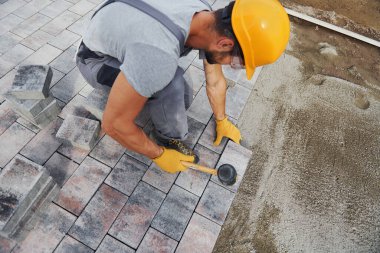 Lastik çekiç kullanıyor. Sarı üniformalı erkek işçi kaldırımda çalışıyor..