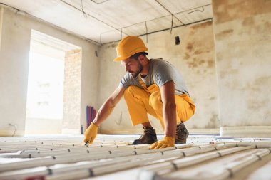 Sarı üniformalı işçiler zemin altı ısıtma sistemi kuruyor.