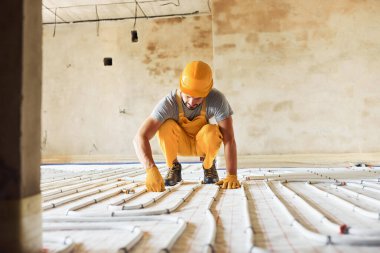 Sarı üniformalı işçiler zemin altı ısıtma sistemi kuruyor.