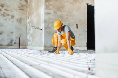 Sarı üniformalı işçiler zemin altı ısıtma sistemi kuruyor.