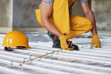 Manzarayı kapat. Sarı üniformalı işçiler zemin altı ısıtma sistemi kuruyor.