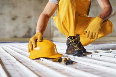 Kasketli. Sarı üniformalı işçiler zemin altı ısıtma sistemi kuruyor.