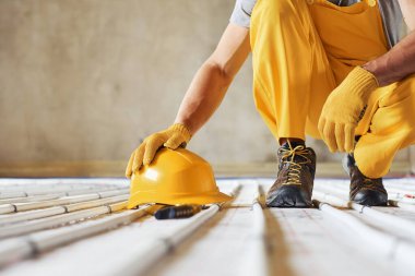 Kasketli. Sarı üniformalı işçiler zemin altı ısıtma sistemi kuruyor.