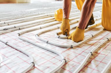 Manzarayı kapat. Sarı üniformalı işçiler zemin altı ısıtma sistemi kuruyor.