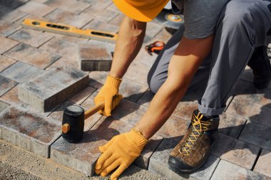 Lastik çekiç kullanıyor. Sarı üniformalı erkek işçi kaldırımda çalışıyor..