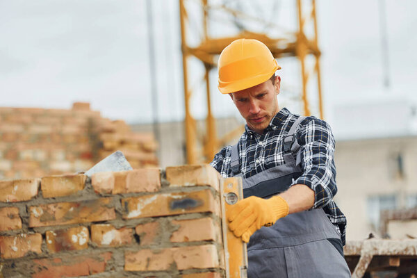 С помощью инструмента контроля уровня. Строитель в форме и технике безопасности имеет работу по строительству.