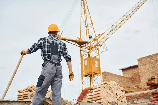 Ellerinde kürekle. Üniformalı inşaat işçisi ve güvenlik ekipmanı inşaatında çalışıyor.