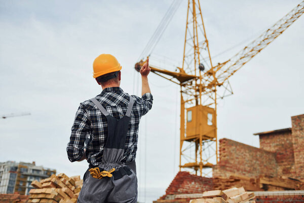 Communicates with the crane driver. Construction worker in uniform and safety equipment have job on building.