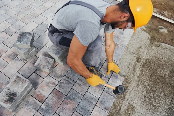 Lastik çekiç kullanıyor. Sarı üniformalı erkek işçi kaldırımda çalışıyor..