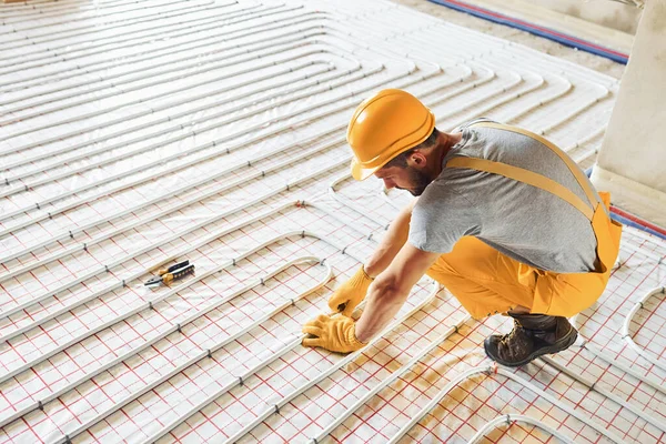 Sarı üniformalı işçiler zemin altı ısıtma sistemi kuruyor.