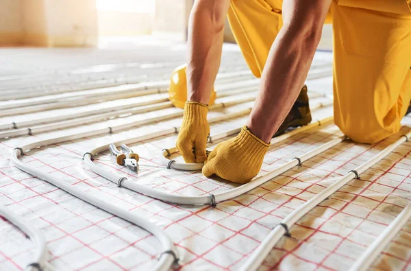 Bir sürü boru. Sarı üniformalı işçiler zemin altı ısıtma sistemi kuruyor.