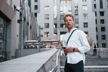 Akıllı telefon ellerde. Şık giyinmiş genç bir adam gündüz vakti şehir dışında..