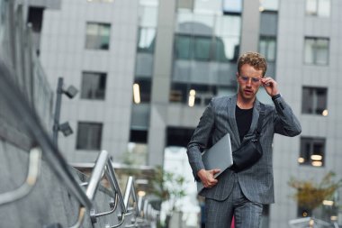 Laptop ellerde. Şık giyinmiş genç bir adam gündüz vakti şehir dışında..