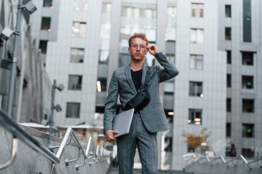 Laptop ellerde. Şık giyinmiş genç bir adam gündüz vakti şehir dışında..