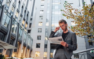 Gazete okuyor. Şık giyinmiş genç bir adam gündüz vakti şehir dışında..
