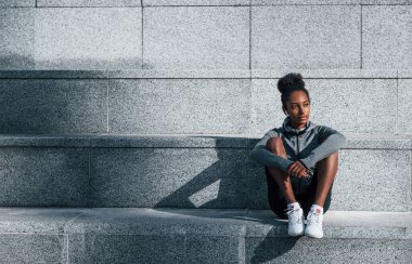 Merdivenlerde oturuyor. Spor elbiseli genç Afrikalı Amerikalı kadın gündüzleri dışarıda antrenman yapıyor..