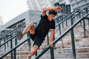 Parkur yapıyor. Spor elbiseli genç adam gündüz vakti dışarıda antrenman yapıyor..