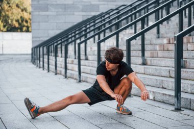 Esniyor ve hazırlanıyor. Spor elbiseli genç adam gündüz vakti dışarıda antrenman yapıyor..