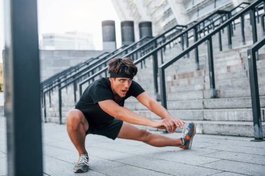 Esniyor ve hazırlanıyor. Spor elbiseli genç adam gündüz vakti dışarıda antrenman yapıyor..