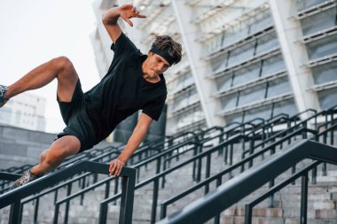 Koşmak ve zıplamak. Spor elbiseli genç adam gündüz vakti dışarıda antrenman yapıyor..