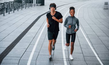Avrupalı erkek ve Afrikalı Amerikalı kadın spor kıyafetleri içinde birlikte spor yapıyorlar..