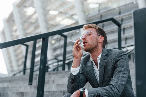 Oturup Sigara Içiyor Gri Üniformalı Genç Başarılı Adamı Şehirde Açık — Stok fotoğraf