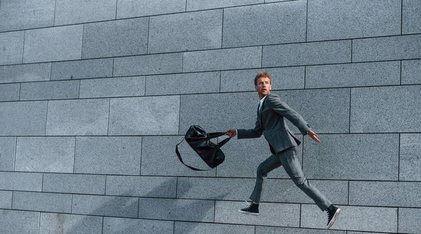 Running and late for the work. Young successful businessman in grey formal wear is outdoors in the city.