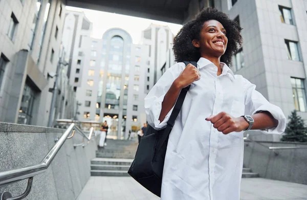 African american woman in good clothes is outdoors in the city at daytime.