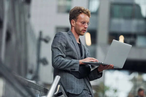 手提电脑在手上 穿着漂亮衣服的年轻而优雅的男子白天在城市的室外 — 图库照片