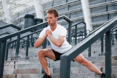 Esniyor ve hazırlanıyor. Spor elbiseli genç adam gündüz vakti dışarıda antrenman yapıyor..