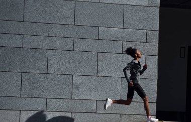 Aktif koşucu. Spor elbiseli genç Afrikalı Amerikalı kadın gündüzleri dışarıda antrenman yapıyor..