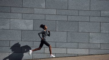 Duvarın yanından geçen spor elbiseli Afrikalı Amerikalı genç bir kadının yan görüntüsü..