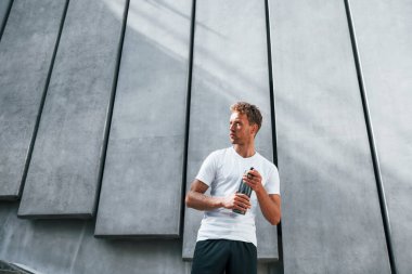 Su içer ve ara verir. Spor elbiseli genç adam gündüz vakti dışarıda antrenman yapıyor..