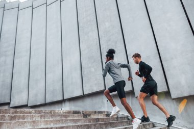 Büyük duvarın yanında. Avrupalı erkek ve Afrikalı Amerikalı kadın spor kıyafetleri içinde birlikte spor yapıyorlar..