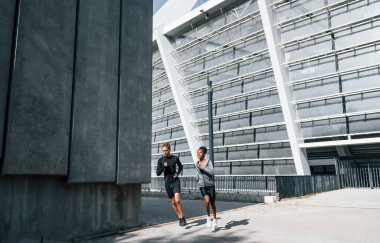 Büyük duvarın yanında. Avrupalı erkek ve Afrikalı Amerikalı kadın spor kıyafetleri içinde birlikte spor yapıyorlar..