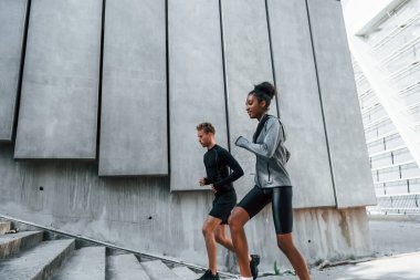 Büyük duvarın yanında. Avrupalı erkek ve Afrikalı Amerikalı kadın spor kıyafetleri içinde birlikte spor yapıyorlar..