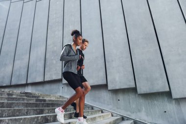 Büyük duvarın yanında. Avrupalı erkek ve Afrikalı Amerikalı kadın spor kıyafetleri içinde birlikte spor yapıyorlar..