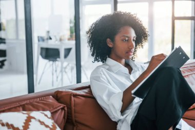 Not defteri tutuyor. Evde kıvırcık saçlı, Afro-Amerikalı bir kadın var..