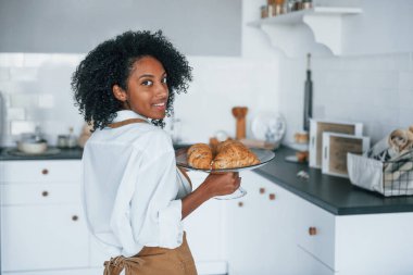 İçinde kruvasan var. Evde kıvırcık saçlı, Afro-Amerikalı bir kadın var..