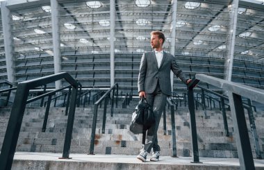 Stadyumun merdivenlerinde. Gri üniformalı genç işadamı şehirde açık havada..