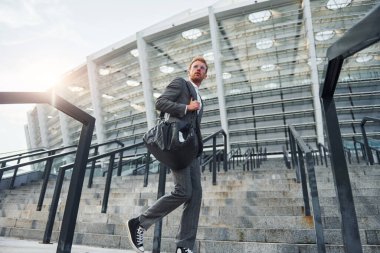 Çantayı elinde tutuyor. Gri üniformalı genç işadamı şehirde açık havada..