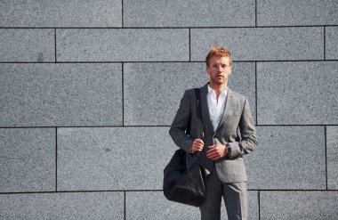 Gri duvara yaslan. Gri üniformalı genç işadamı şehirde açık havada..