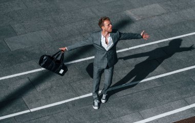 Dans etmek, başarıyı kutlamak. Gri üniformalı genç işadamı şehirde açık havada..