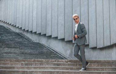 Kamera için poz vermek. Gri üniformalı genç işadamı şehirde açık havada..