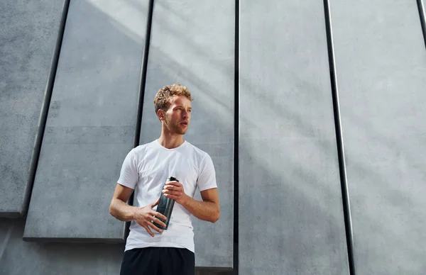 Against building exterior. Young man in sportive clothes have workout outdoors at daytime.