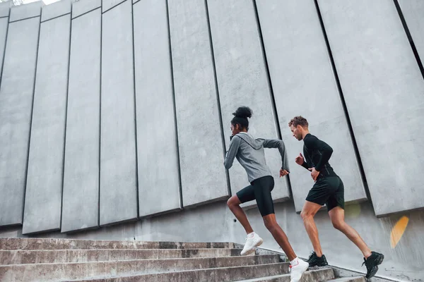 在大墙附近穿着运动服的欧洲男人和非洲女人一起锻炼 — 图库照片