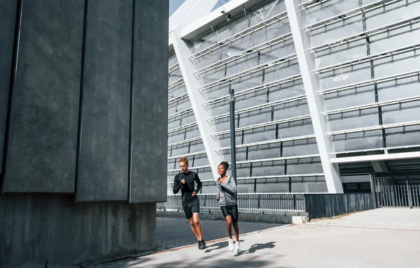在大墙附近穿着运动服的欧洲男人和非洲女人一起锻炼 — 图库照片
