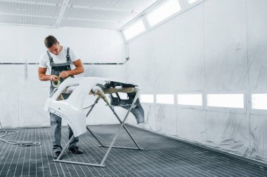 Araba kaputuyla çalışıyor. Garajda üniformalı beyaz araba tamircisi..