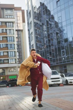 Koşuyor, işe geç kalıyor. Pijamalı genç adam dışarıda, sokakta. Uykulu hissediyorum..