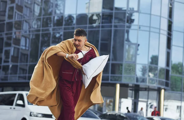 Running, late for the work. Young man in pajama is outdoors on the street. Feels sleepy.